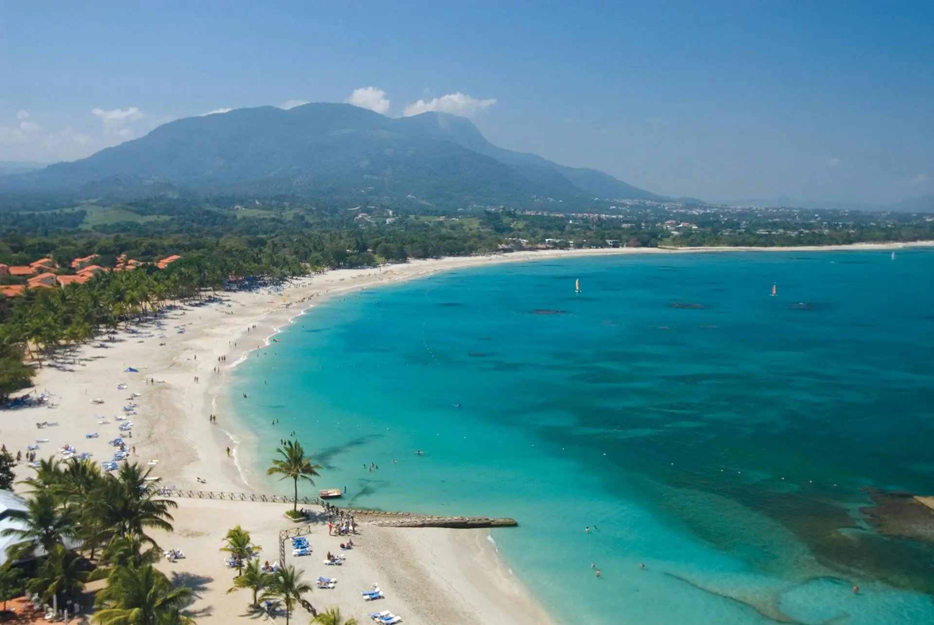 A sweeping sandy coastline, turquoise sea and green mountains